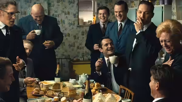A group of suited men laugh around a table laden with tea and food