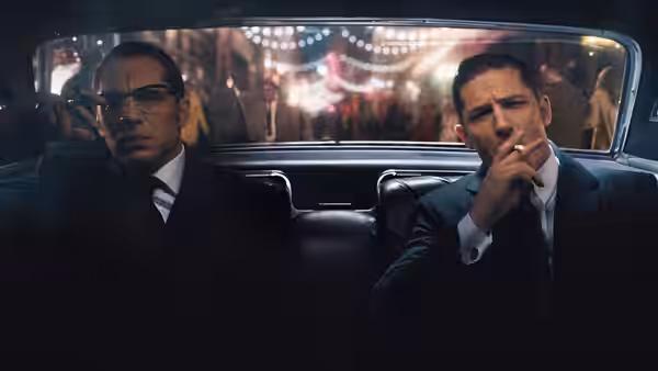 Ronald and Reginald Kray (Tom Hardy) ride in a car, one smoking in the back seat