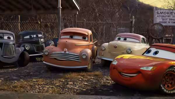 Lightning McQueen meets a group of older cars outside a fenced garage