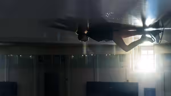 A figure skater glides upside down beneath the reflective ice