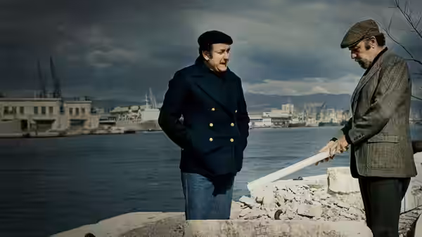 Two men in coats and caps standing by a harbor holding a long white object
