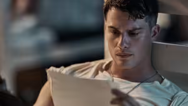 A young man in uniform reads a letter indoors