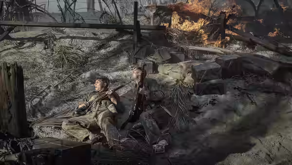 Two soldiers lie wounded in a muddy trench as fire burns behind them