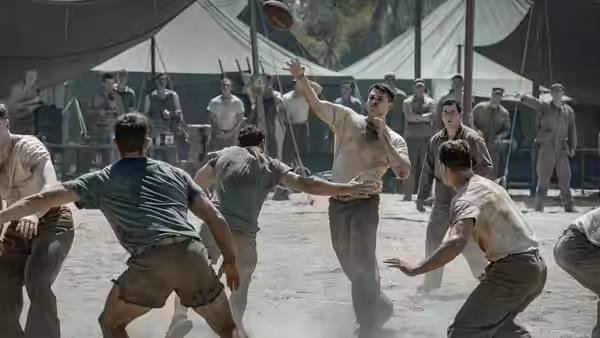 Football players practice passing on a field surrounded by military tents