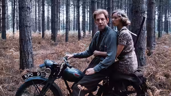A man and woman ride a motorcycle through a sparse forest