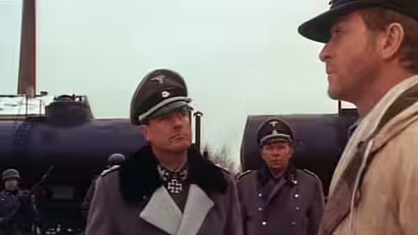 German officers face a man in a light-colored coat beside railway cars