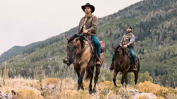 Two mounted marshals cross a rocky meadow below a forested hillside