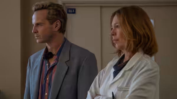 A man and woman stand in a corridor, both looking off to the side