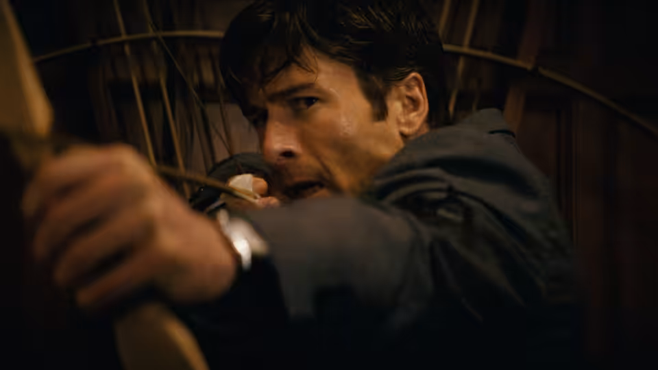 Becket (Glen Powell) aiming a bow and arrow with intense focus