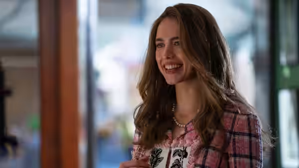Julia (Margaret Qualley) smiling while wearing a pink plaid jacket