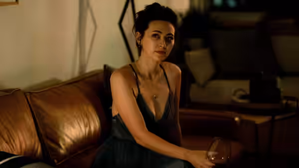 Ruth (Jessica Henwick) seated on a couch holding a wine glass