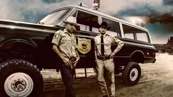 Lt. Joe Leaphorn (Zahn McClarnon) and Jim Chee (Kiowa Gordon) stand beside a Navajo Police vehicle