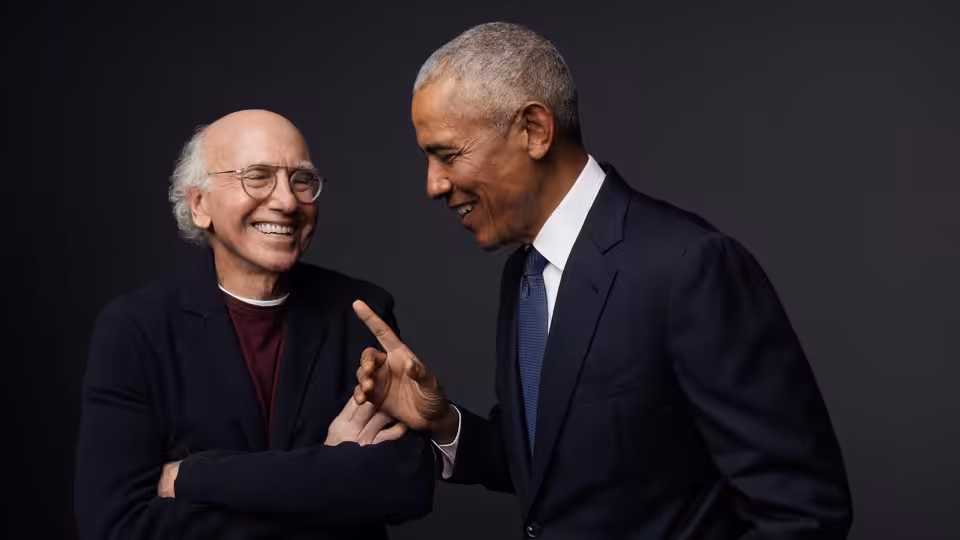 Larry David and Barack Obama smile as Obama gestures toward David's hand
