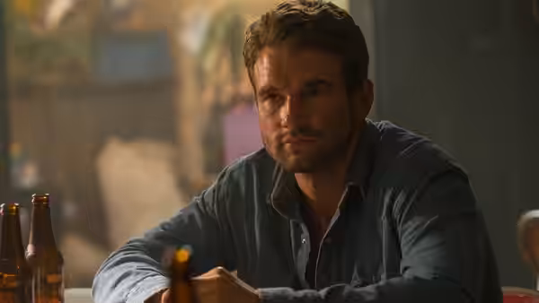 Kevin (Alex Russell) sits at a table with bottles nearby