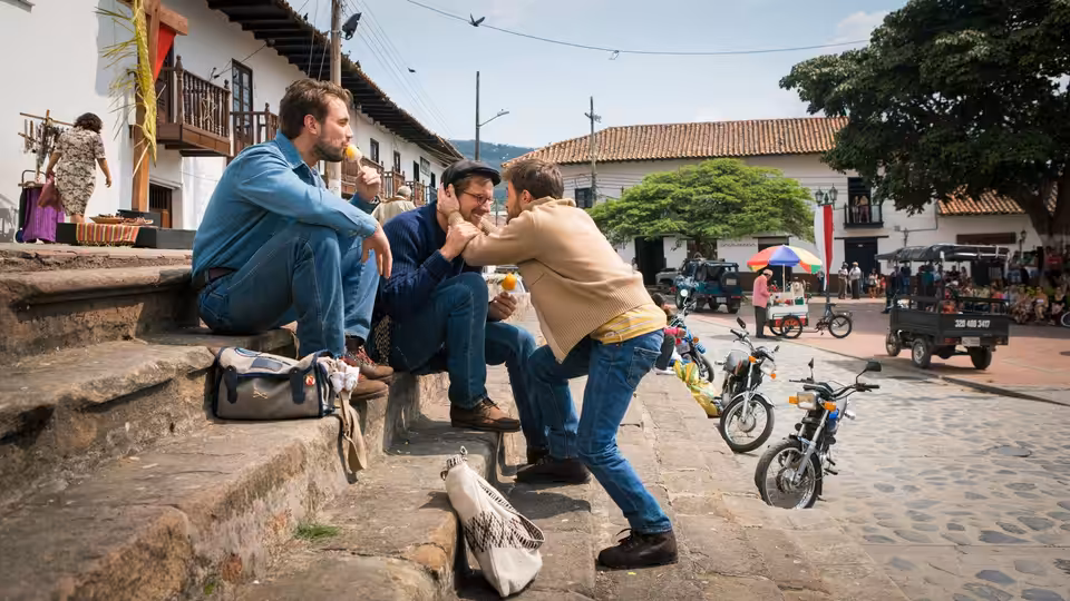 Two travelers greet each other on stone steps beside a busy town street