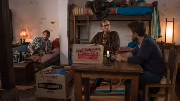 Three travelers gather around a table in a bunkroom