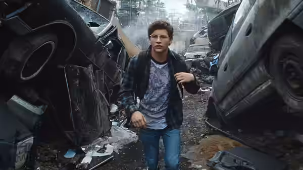 Wade (Tye Sheridan) walks between piled vehicles in a junkyard