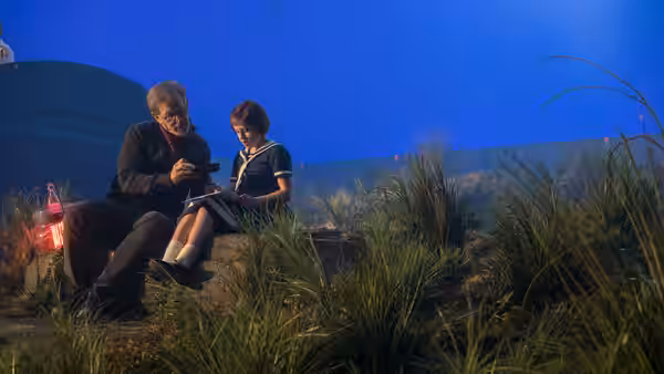The BFG (Mark Rylance) sits beside Sophie (Ruby Barnhill) among tall grass beneath a blue sky