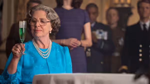 The Queen (Penelope Wilton) raises a glass while attendants stand behind her