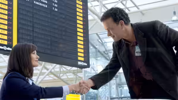 Viktor Navorski (Tom Hanks) shakes hands with Amelia Warren (Catherine Zeta-Jones) beneath airport departure boards