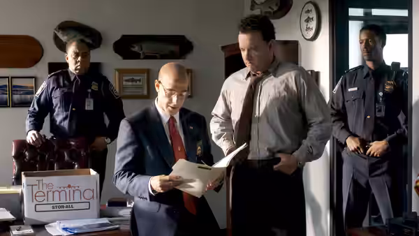 Viktor Navorski (Tom Hanks) stands beside Frank Dixon (Stanley Tucci) as he reads papers in an office