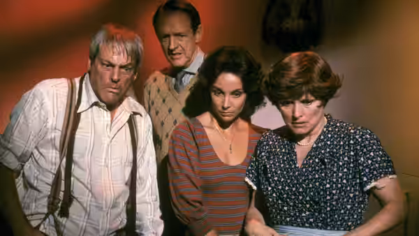 Four people stand together, looking down with tense expressions