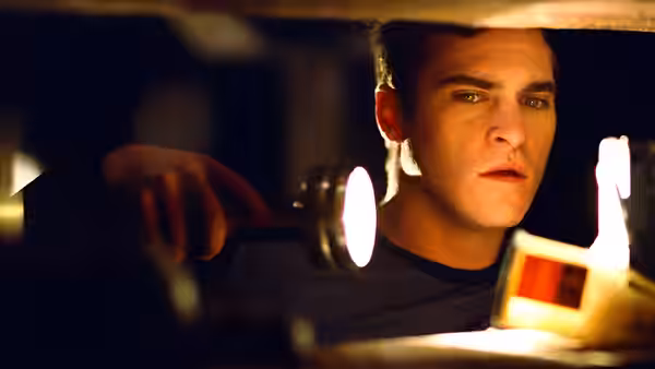 A man peers through a narrow opening as light spills into the dark room