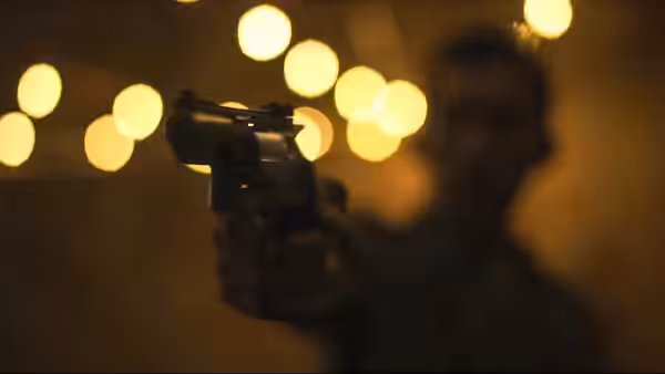 A shadowed figure raises a handgun against blurred lights