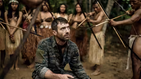 A seated man looks up as women and men hold sticks around him