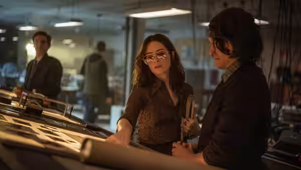 Two women examine a newspaper layout at a newsroom desk