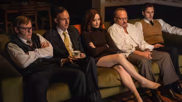 Five colleagues sit together on an office sofa, listening and talking