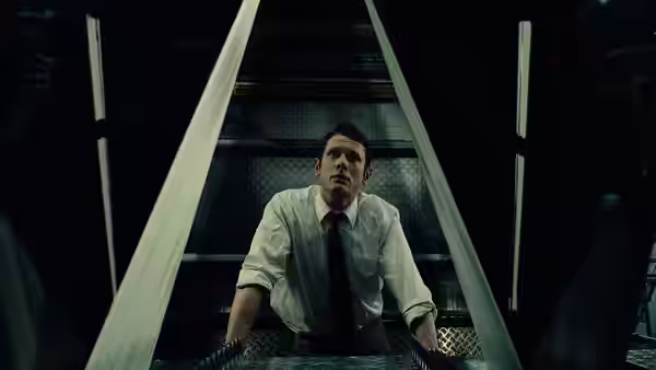 A man leans on a railing inside a dark, industrial elevator