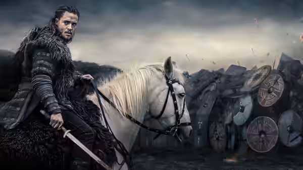 Uhtred of Bebbanburg (Alexander Dreymon) holds a sword beside a white horse and shield-lined wagons
