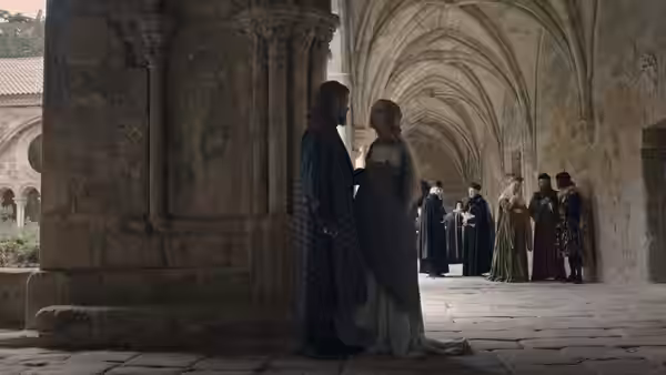 A man and woman stand beneath a stone archway as attendants gather in the corridor