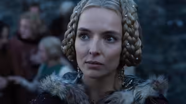Marguerite de Carrouges (Jodie Comer) watches from a crowded gathering, wearing a braided headdress