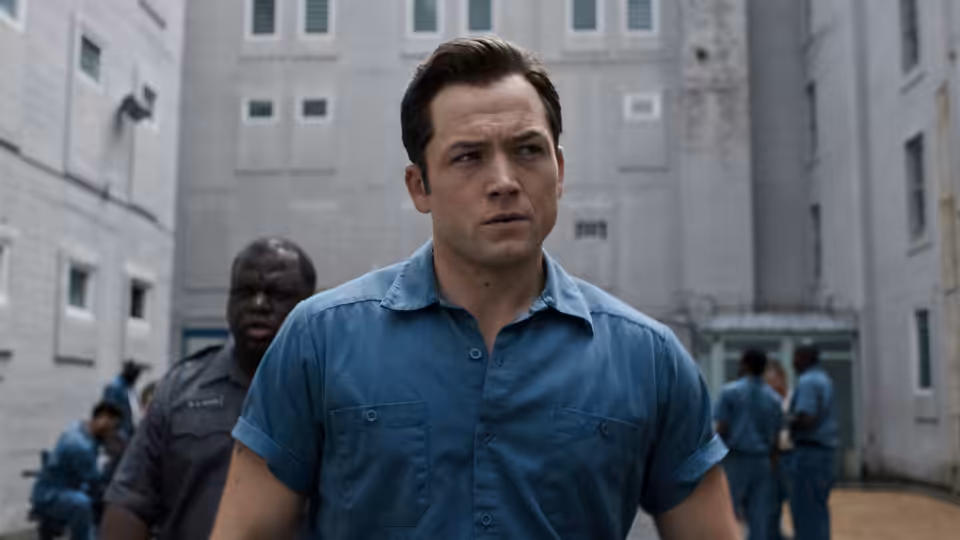 James Keene (Taron Egerton) walks through a prison yard as inmates gather behind him