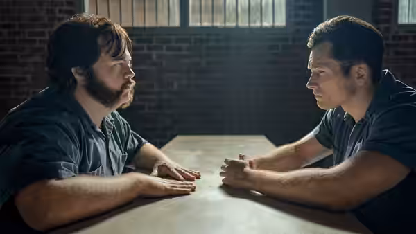 Larry Hall (Paul Walter Hauser) and James Keene (Taron Egerton) sit across a table in prison
