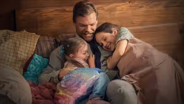 Ed Schmitt (Alan Ritchson) cuddles his two daughters beneath blankets on a bed