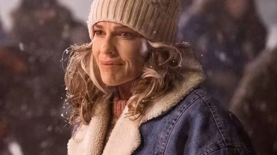 Sharon Stevens (Hilary Swank) in a knit hat and winter coat outdoors in falling snow