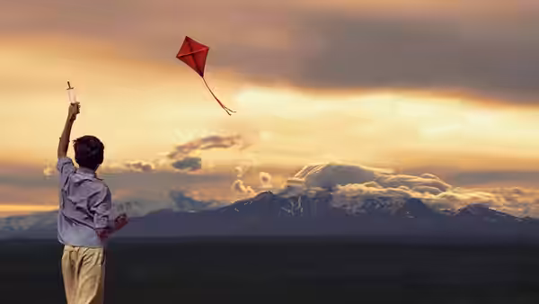 Young Amir flies a red kite against a sunset over the mountains