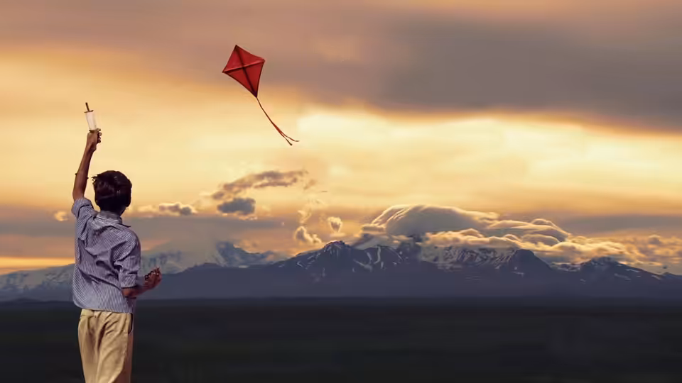 Young Amir flies a red kite against a sunset over the mountains