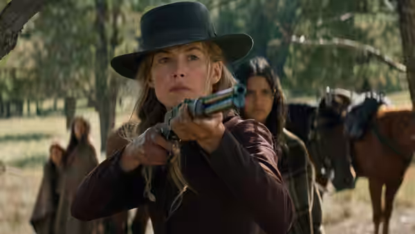 Rosalee Quaid (Rosamund Pike) aims a rifle beneath a covered wagon as a horse stands nearby