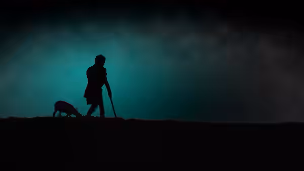 A lone figure walks across a dark ridge as a dog follows