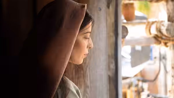 A veiled woman gazes down beside a sunlit window