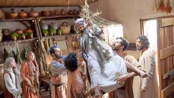 A man in a white robe is lifted above a crowd inside a room