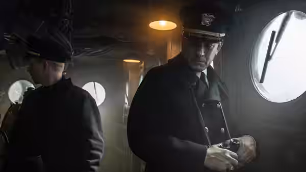 Commander Krause (Tom Hanks) examines an instrument on the dimly lit ship’s bridge