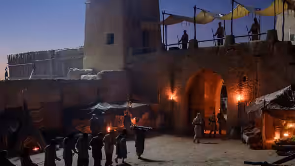 Soldiers guard a fortress courtyard as figures gather beneath the illuminated archway