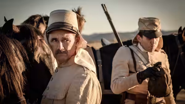A uniformed officer stands among soldiers and prisoners in the open desert