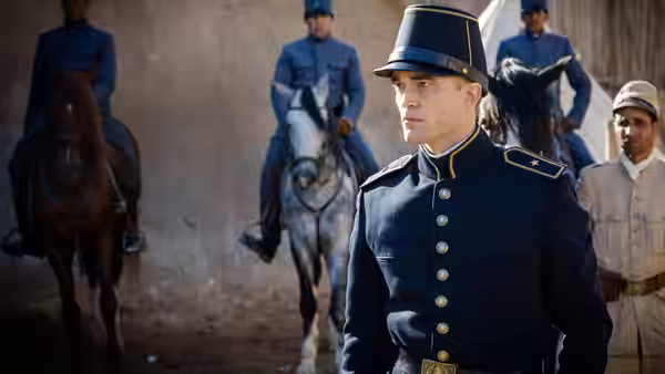 A uniformed officer stands before mounted soldiers inside a stone compound