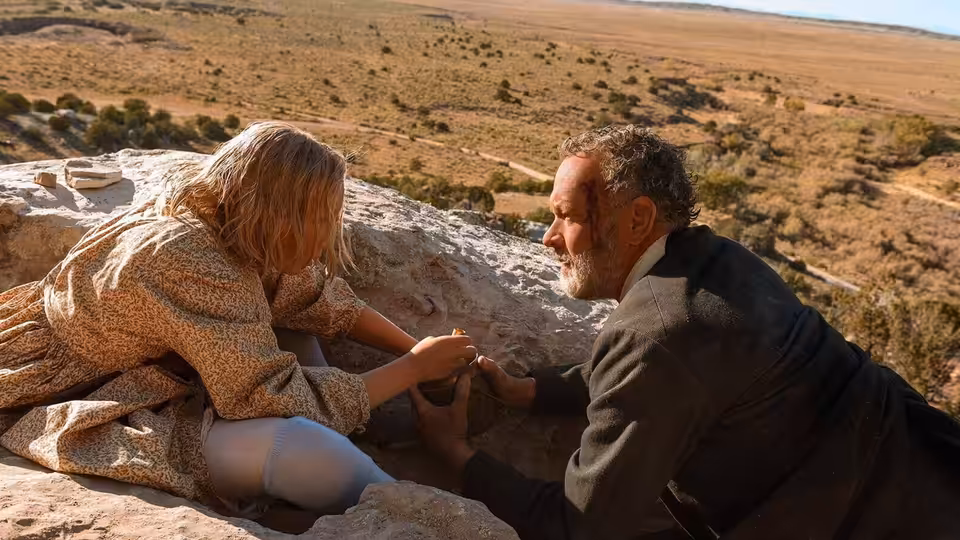 Captain Jefferson Kyle Kidd (Tom Hanks) reaches toward Johanna on a rocky hillside